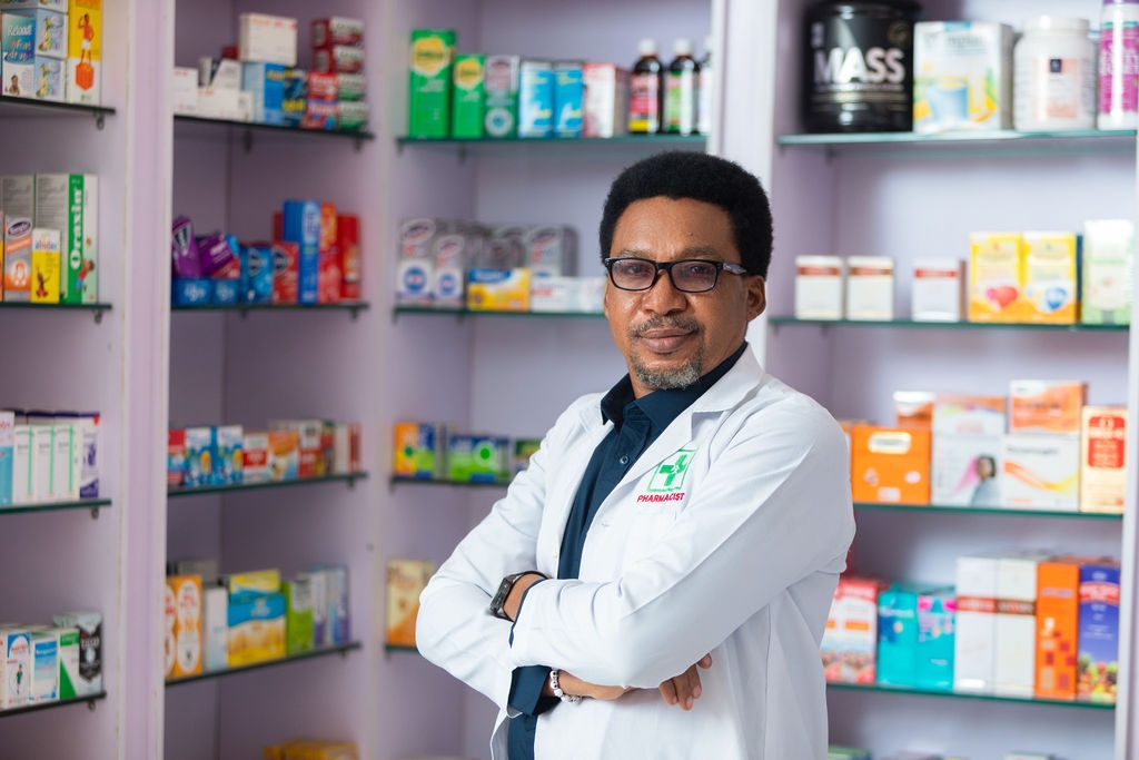 Man in a pharmacy wearing a lab coat and folding his hands